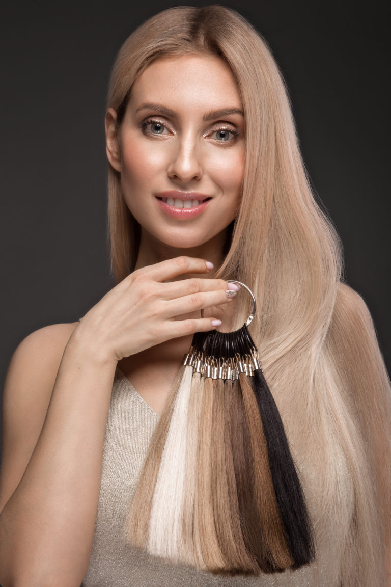 Beautiful blond girl with a perfectly smooth hair, classic make-up with a palette for hair extensions in the hands. Beauty face. Picture taken in the studio.
